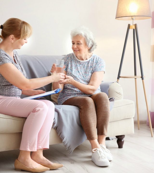 Caregiver giving glass of water to senior woman at home